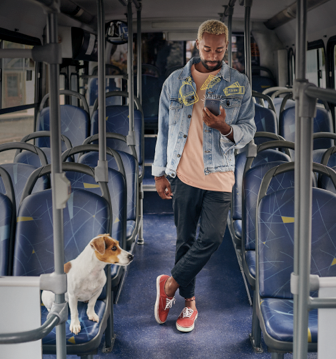 Un homme debout dans un bus, regardant son téléphone pendant que le chien est assis sur un siège