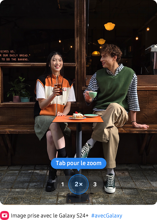 Une photo riche en couleurs de deux personnes assises devant un café prise à un zoom 2x.