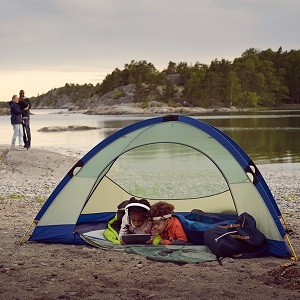 Deux enfants regardant une tablette sous une tente près d'un lac avec des parents à distance